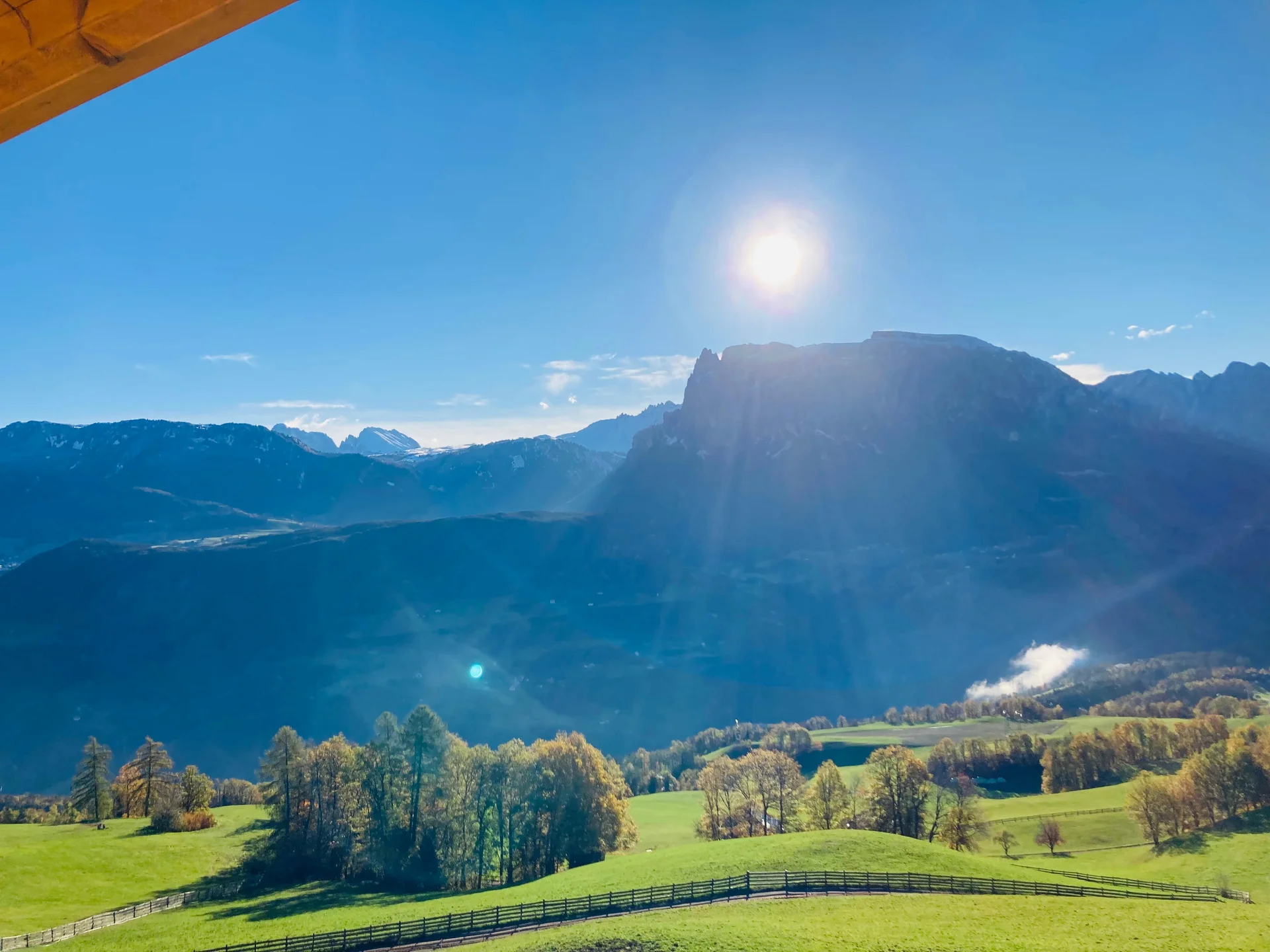 Ferienwohnung am Ritten: Armonia, Hof mit Musik Sonnige Aussicht auf alpine Berge über grünen Wiesen und einem Holzzaun